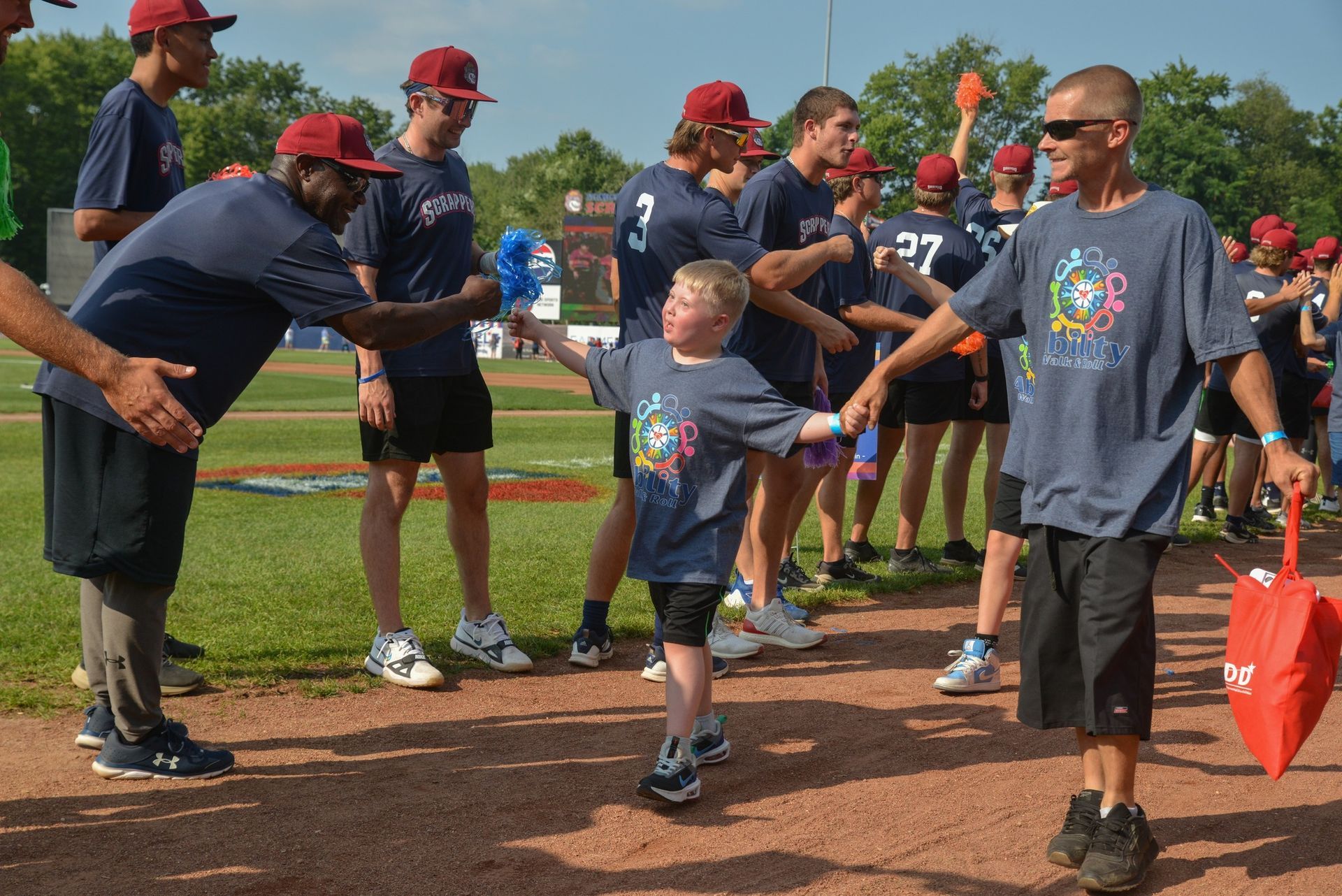 Boy high-fives a man on a baseball field, surrounded by others in matching shirts and hats.