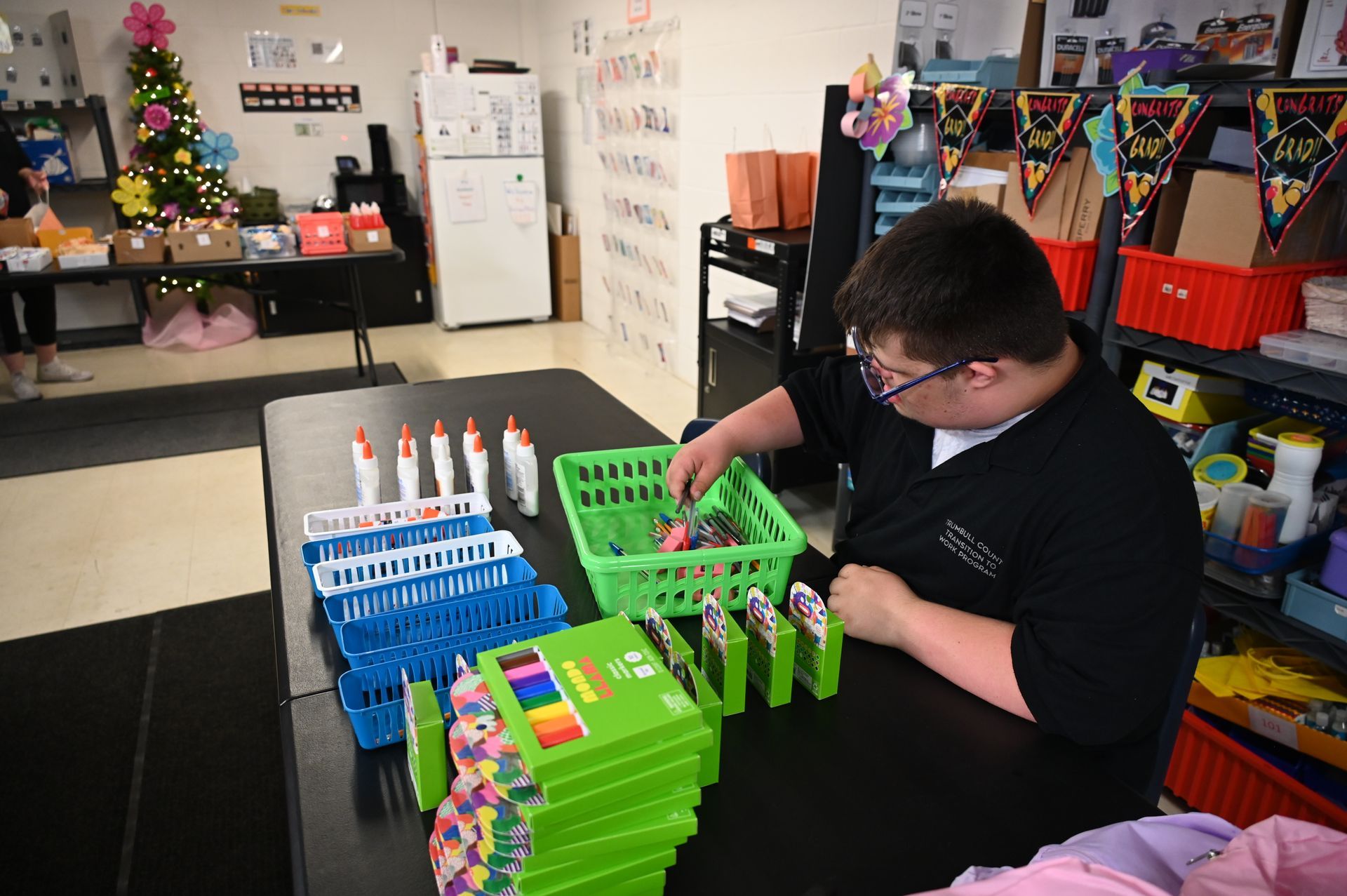 Person with glasses sorting items at a table with organized supplies in a room.