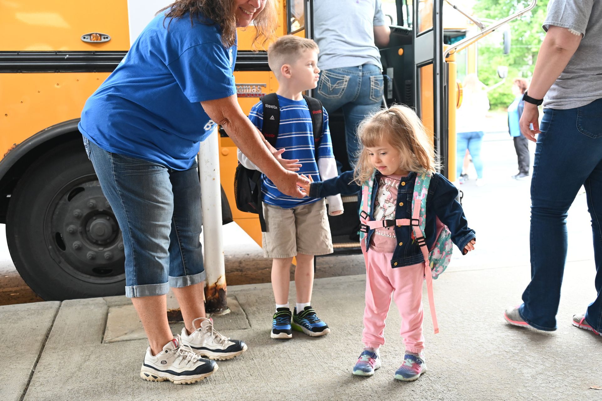 Adult helping young children board a yellow school bus.