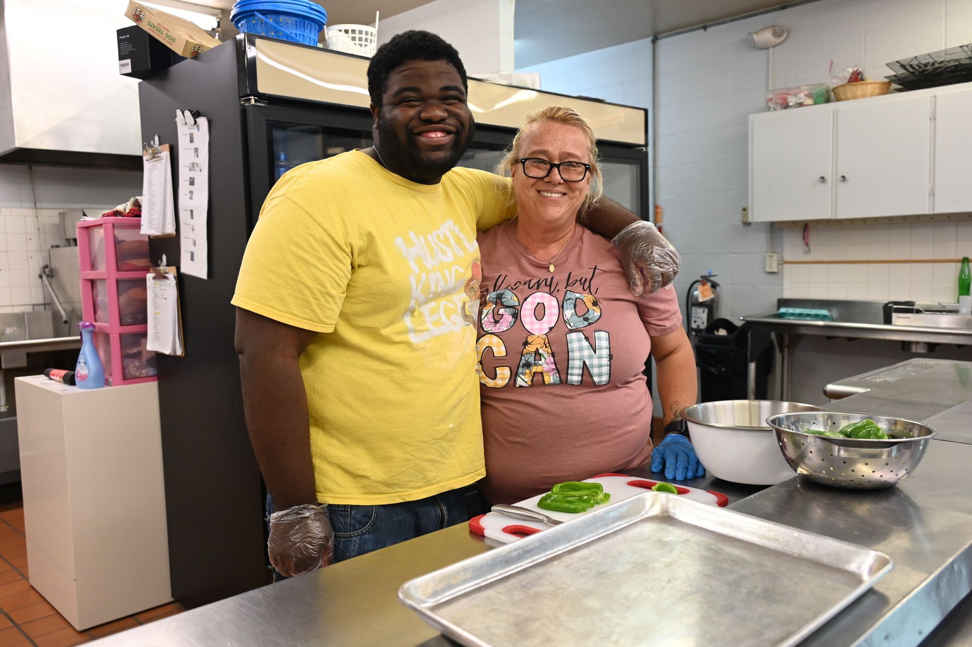 Two people smiling in a commercial kitchen. A person has their arm around another person. 
