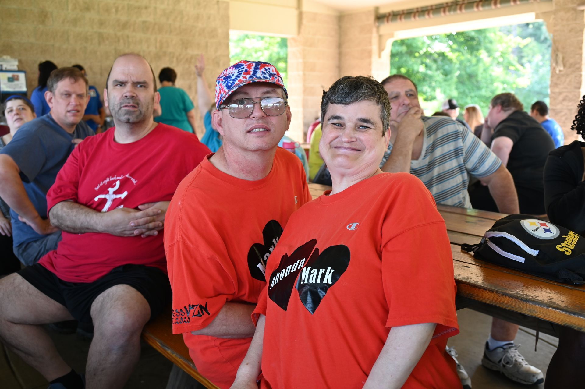 People in red shirts smiling at an outdoor event. Others in background.