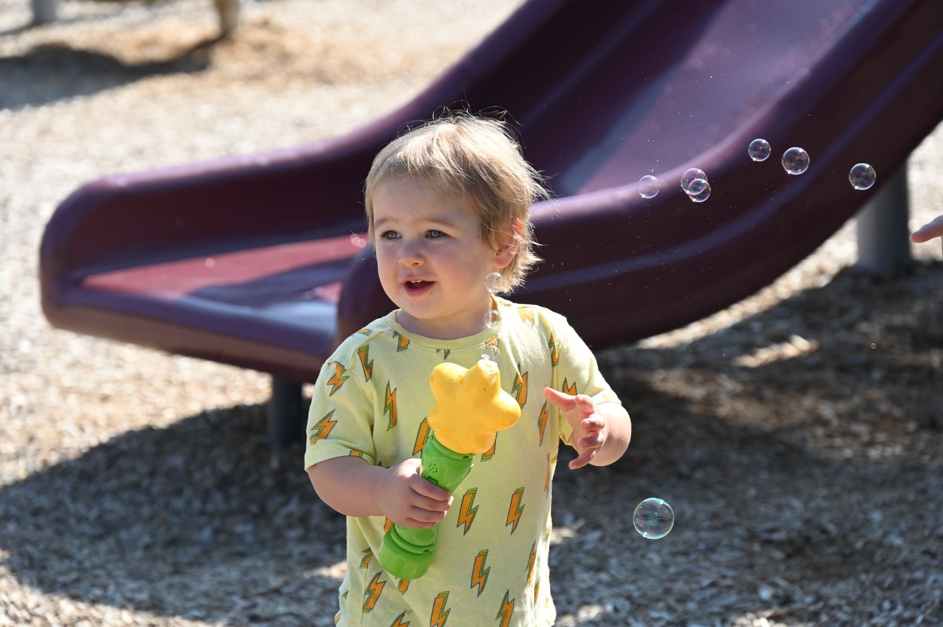 Child playing with a bubble wand near a playground slide.