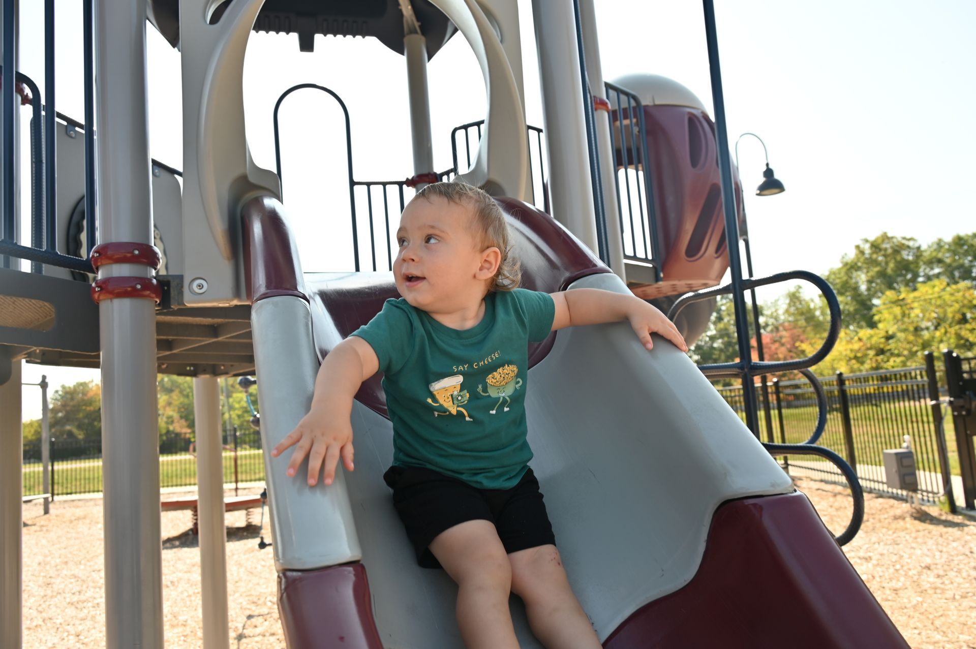 Child sliding down a playground slide, looking to the side with a smile.