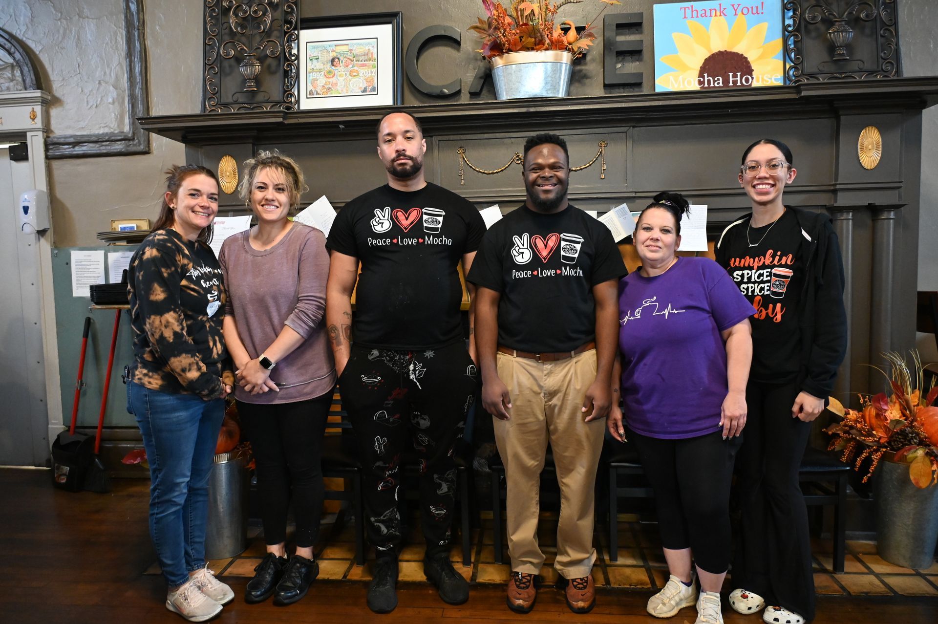 Group of six people standing in front of a cafe counter with fall decorations.