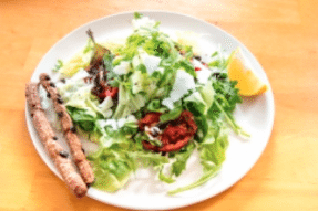 Salad with breadsticks, orange wedge, and dressing on white plate, wooden table.