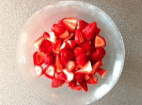 Bowl of chopped red strawberries on a gray surface.