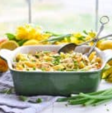 Casserole dish with pasta and vegetables; spoon in dish; yellow flowers in background.