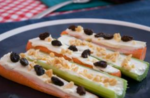 Carrot and celery sticks filled with cream cheese, raisins, and chopped nuts on a blue plate.