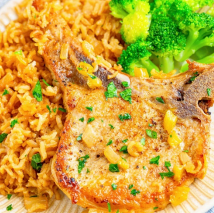 Pork chop with rice and broccoli on a plate, garnished with chopped herbs.