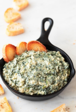 Spinach dip in black skillet with toasted bread slices.