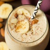 Banana smoothie with banana slices, nuts, and a straw.