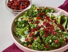 Kale salad with cranberries, sunflower seeds, and dressing in a pink bowl.