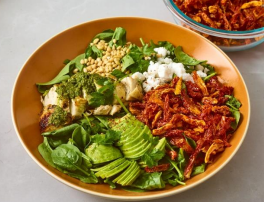 Chicken salad with avocado, sun-dried tomatoes, and pesto in an orange bowl.