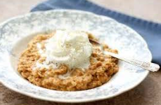 Oatmeal in ornate bowl topped with cream, next to a spoon.