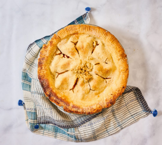 Baked apple pie on a checkered cloth, sitting on a marble surface.