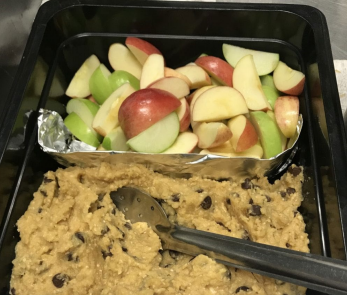 Tray of sliced red and green apples, cookie dough with chocolate chips, and serving tongs.