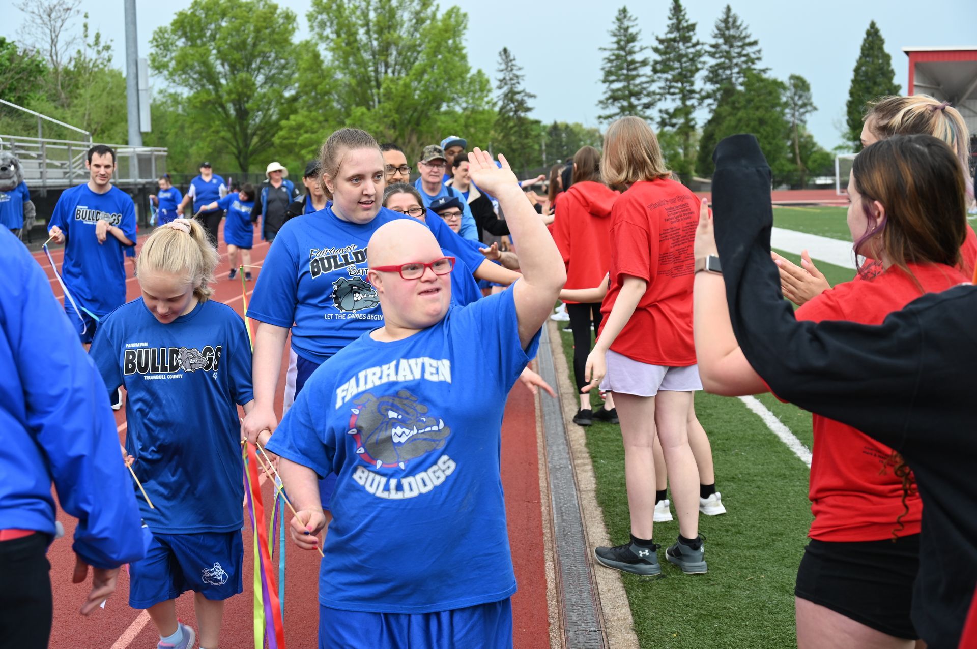 People in blue shirts on a track, one giving a high five, others cheering.
