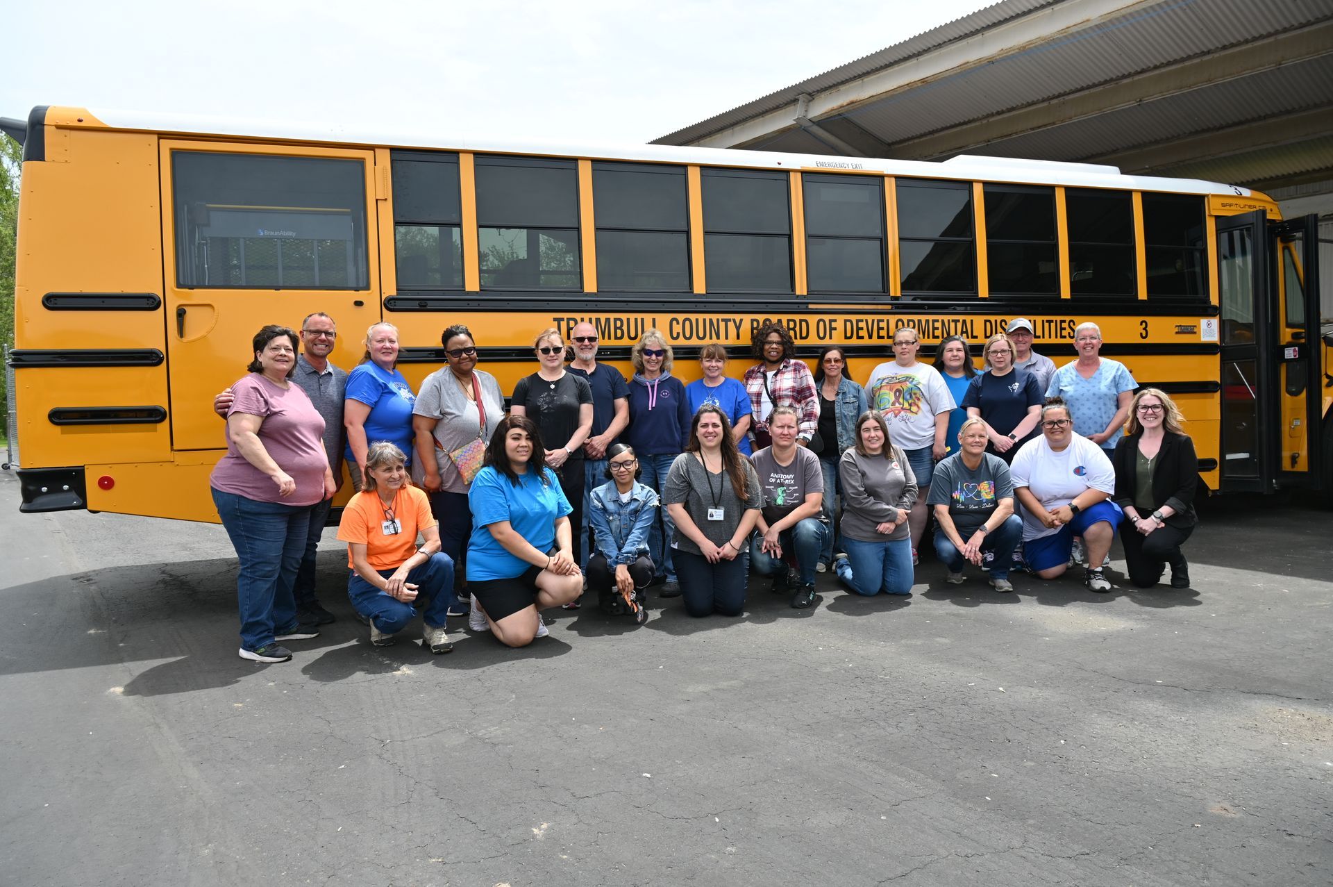Group of people posing by a yellow school bus with open door in an outdoor setting.