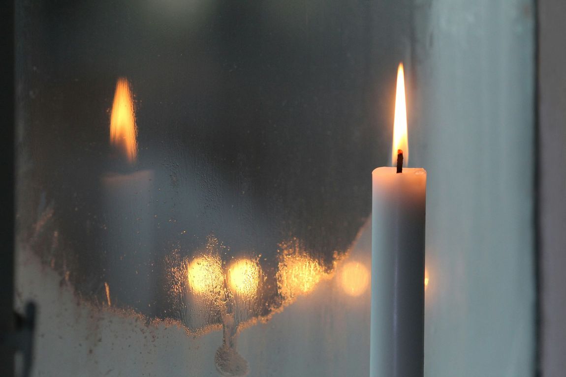 Lit white candle by a window, with warm reflections in the glass