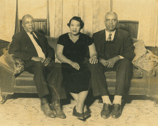 Three adults sit on a couch in a vintage sepia-toned portrait.