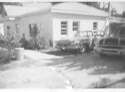 A small house with two parked cars in a driveway and a front yard with bushes.