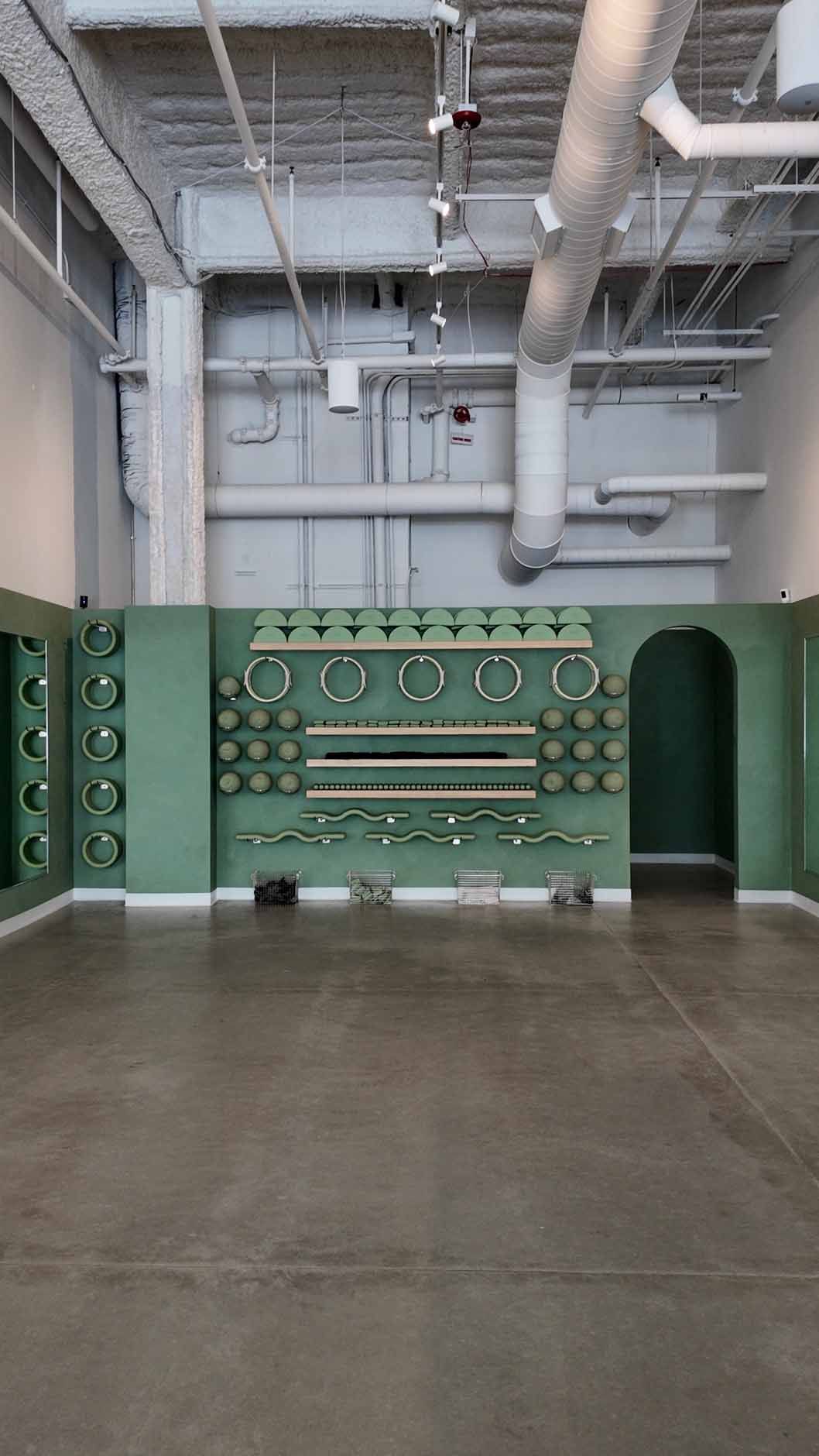 An empty room with a green wall featuring clocks and a curved archway. Beige walls, gray floor.