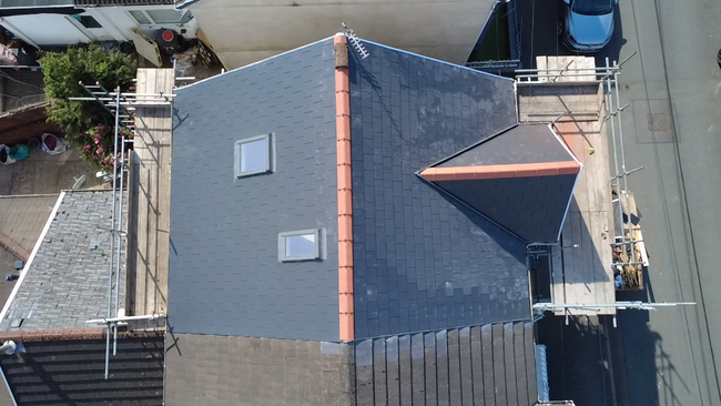 Rooftop with dark shingles and a view of neighboring houses and trees beyond.
