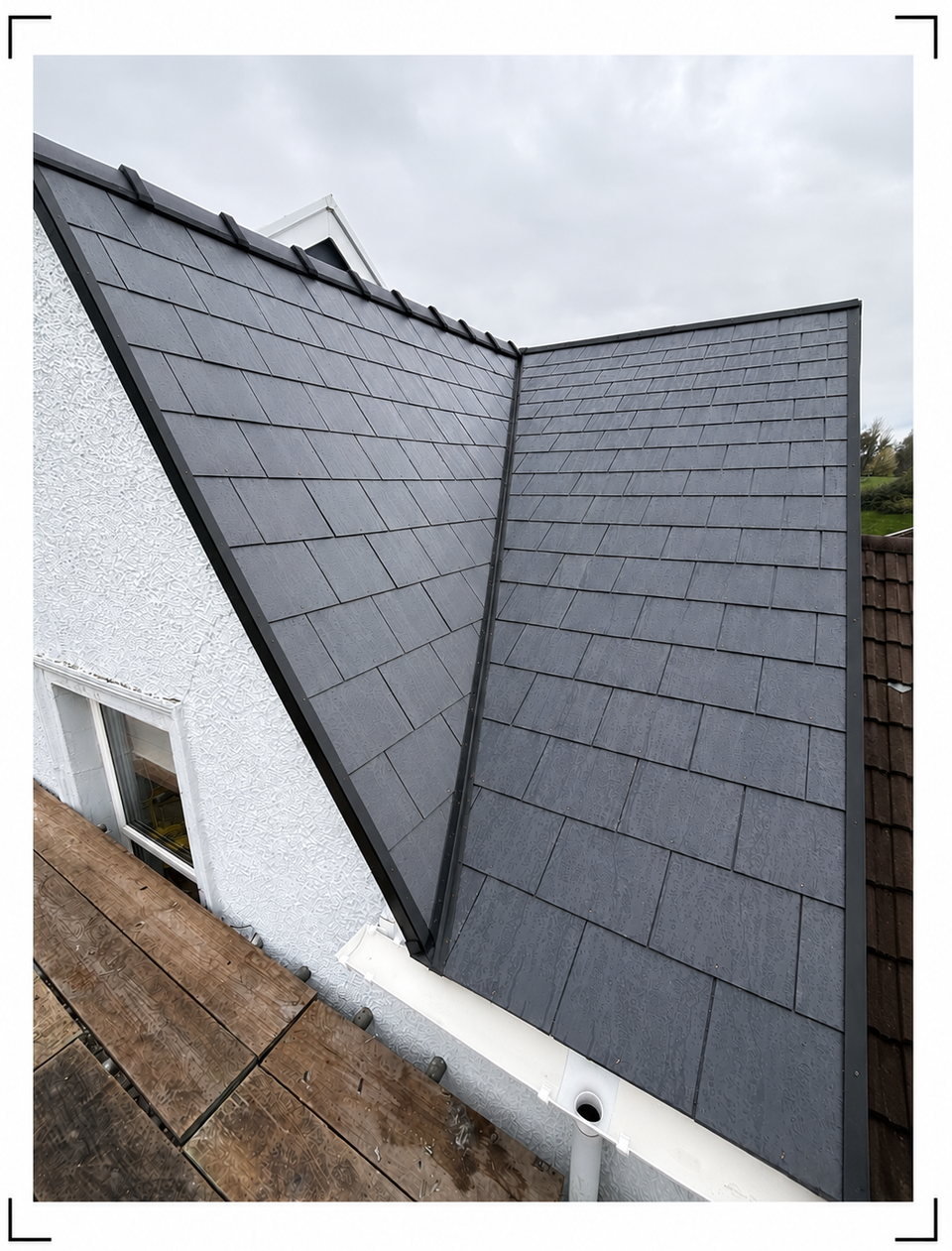 Gray slate roof valleys on a white house under an overcast sky