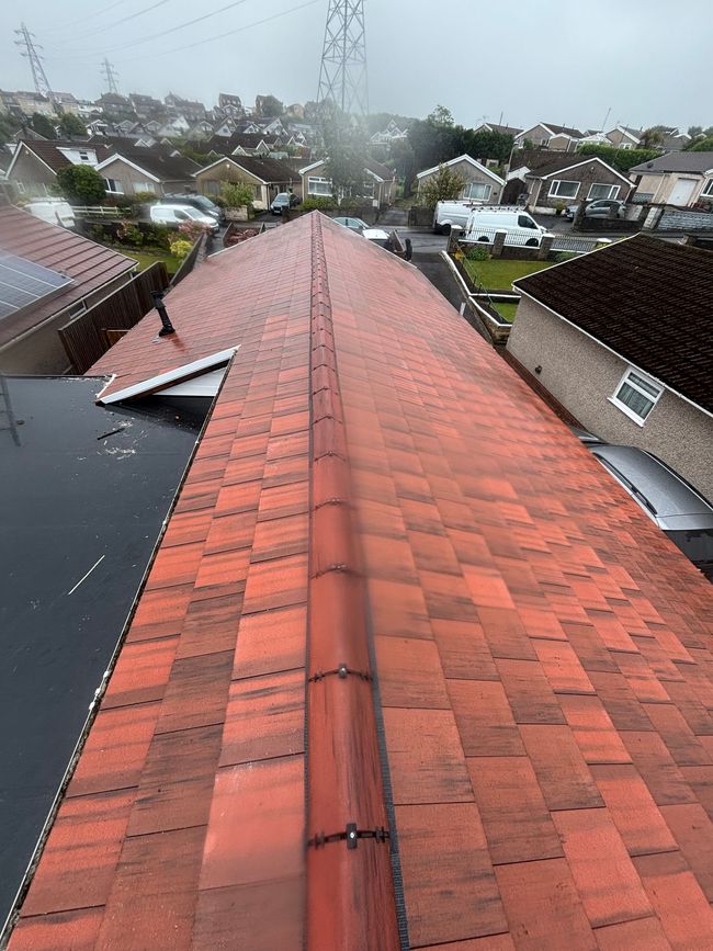 Rooftop with dark shingles and a view of neighboring houses and trees beyond.