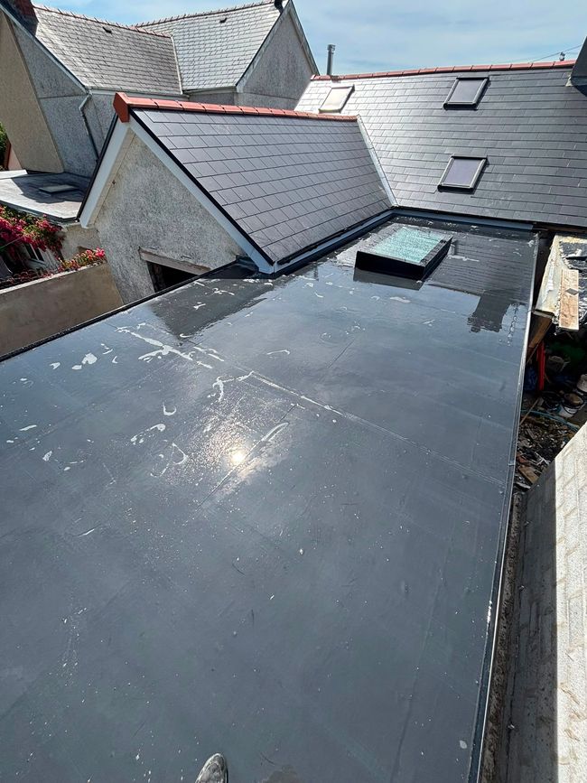 Rooftop with dark shingles and a view of neighboring houses and trees beyond.