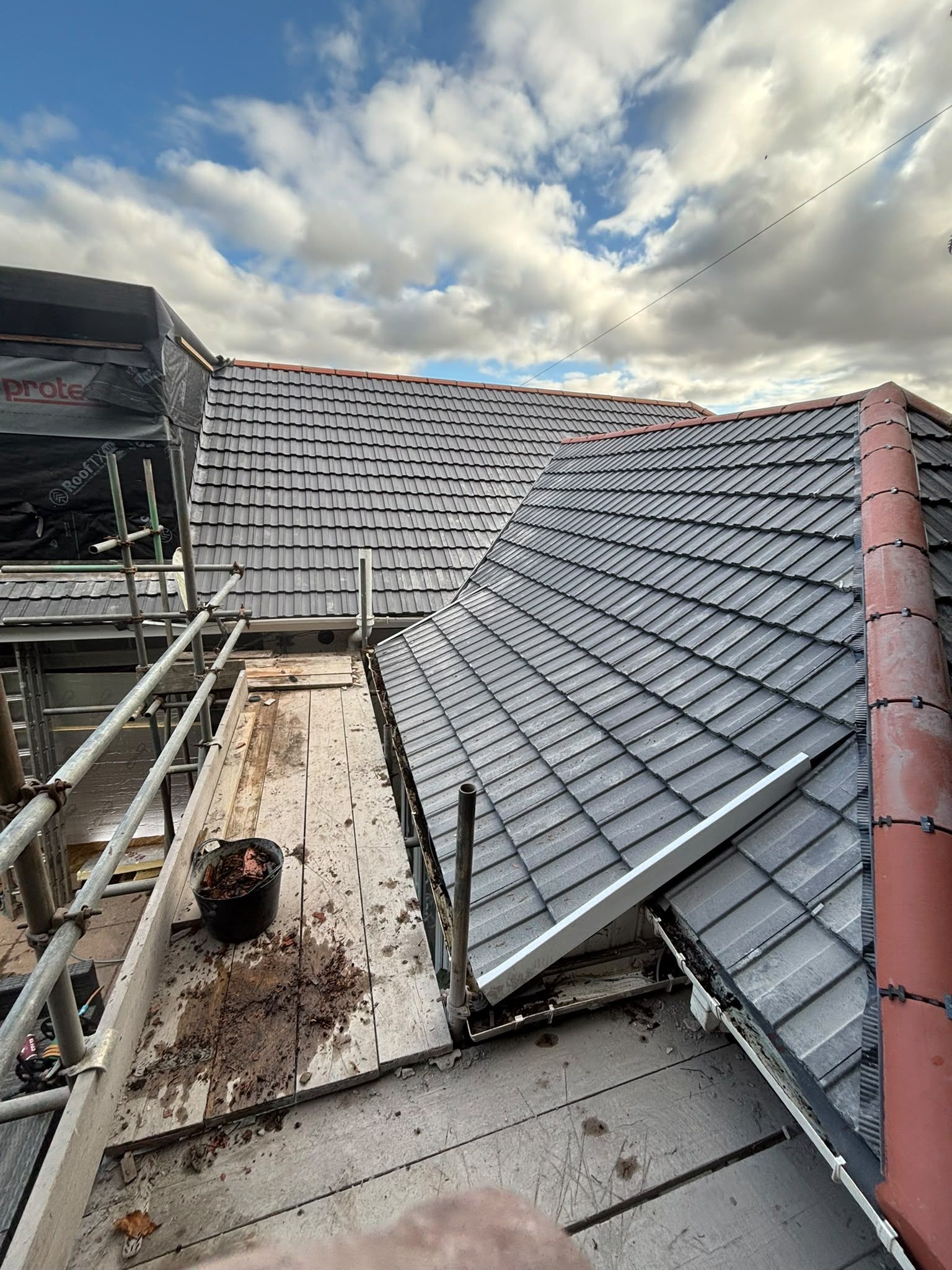 Damaged gray-tiled roof with debris and a cloudy sky, viewed from a rooftop walkway