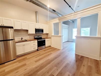 Bright modern kitchen with stainless steel appliances, white cabinets, and light wood floors.