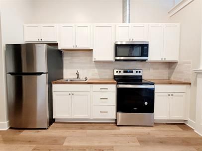 Bright white kitchen with stainless steel fridge, oven, microwave, and wood countertops
