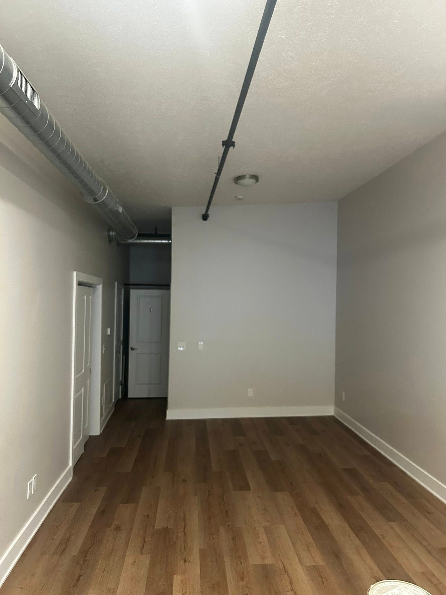 Empty hallway with wood floors, gray walls, and exposed black ceiling track lighting.