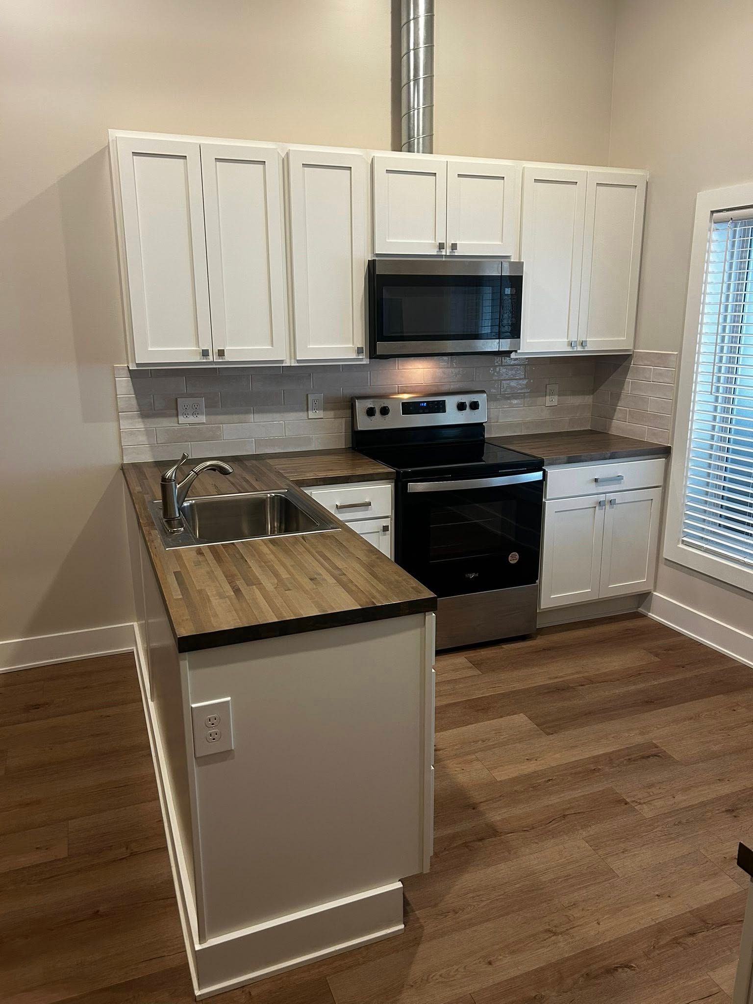 Small kitchen with white cabinets, black appliances, and wood countertops in a vacant apartment