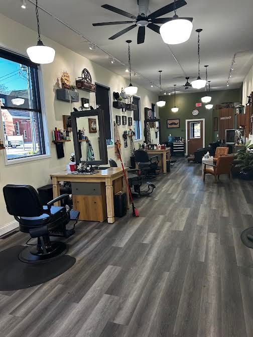 Barbershop interior with black styling chairs, mirrors, pendant lights, and wood-look flooring