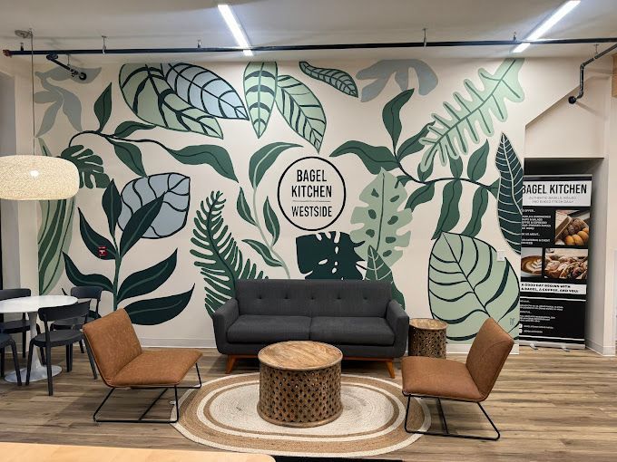 Lounge seating area with leafy wall mural, gray sofa, tan chairs, and round wicker coffee table