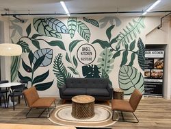 Lounge seating area with leafy wall mural, gray sofa, tan chairs, and round wicker coffee table