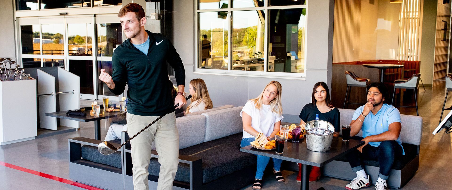 A man is standing in front of a group of people sitting at tables in a restaurant.