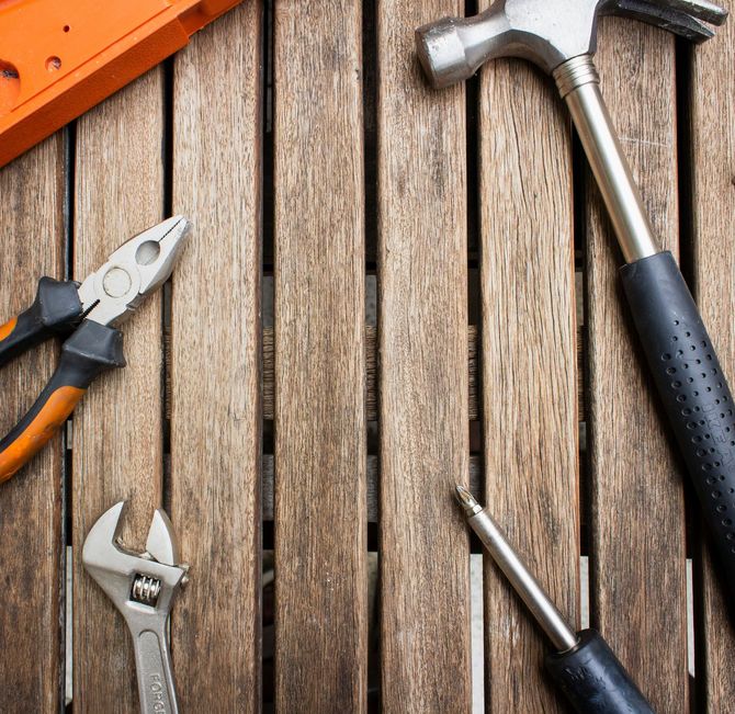 Assorted hand tools on weathered wooden planks, including pliers, wrench, hammer, and screwdriver.