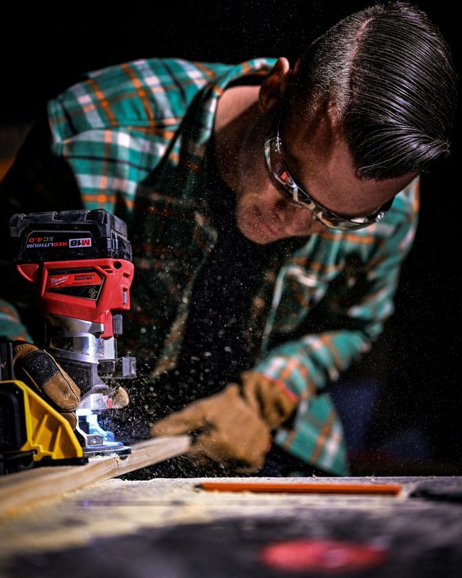 Worker using a red power saw cutting wood, with sawdust flying in a workshop