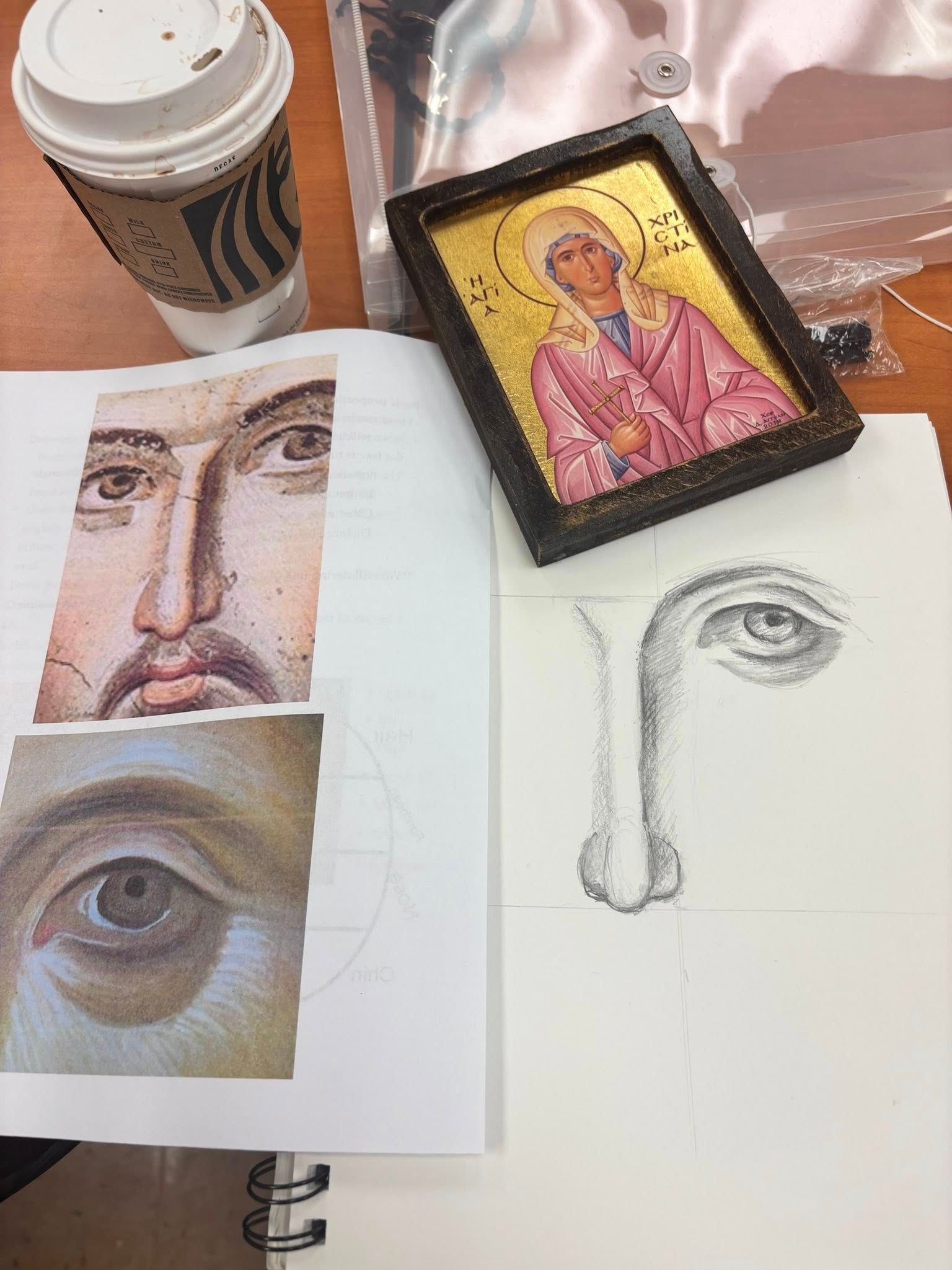 Art study workspace with coffee, sketchbook eye and face drawings, and a small framed icon painting
