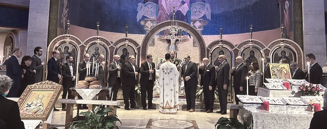 People gathered on a decorated stage in a large ornate hall, with arches and floral arrangements behind them.