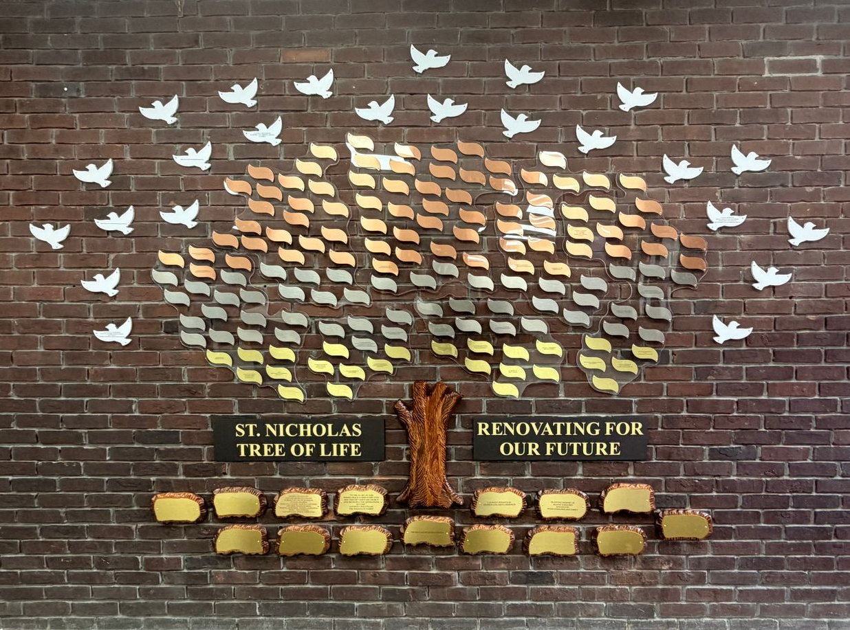 Brick wall memorial with white dove cutouts and yellow paper messages reading “Stand as a tree of life” and 