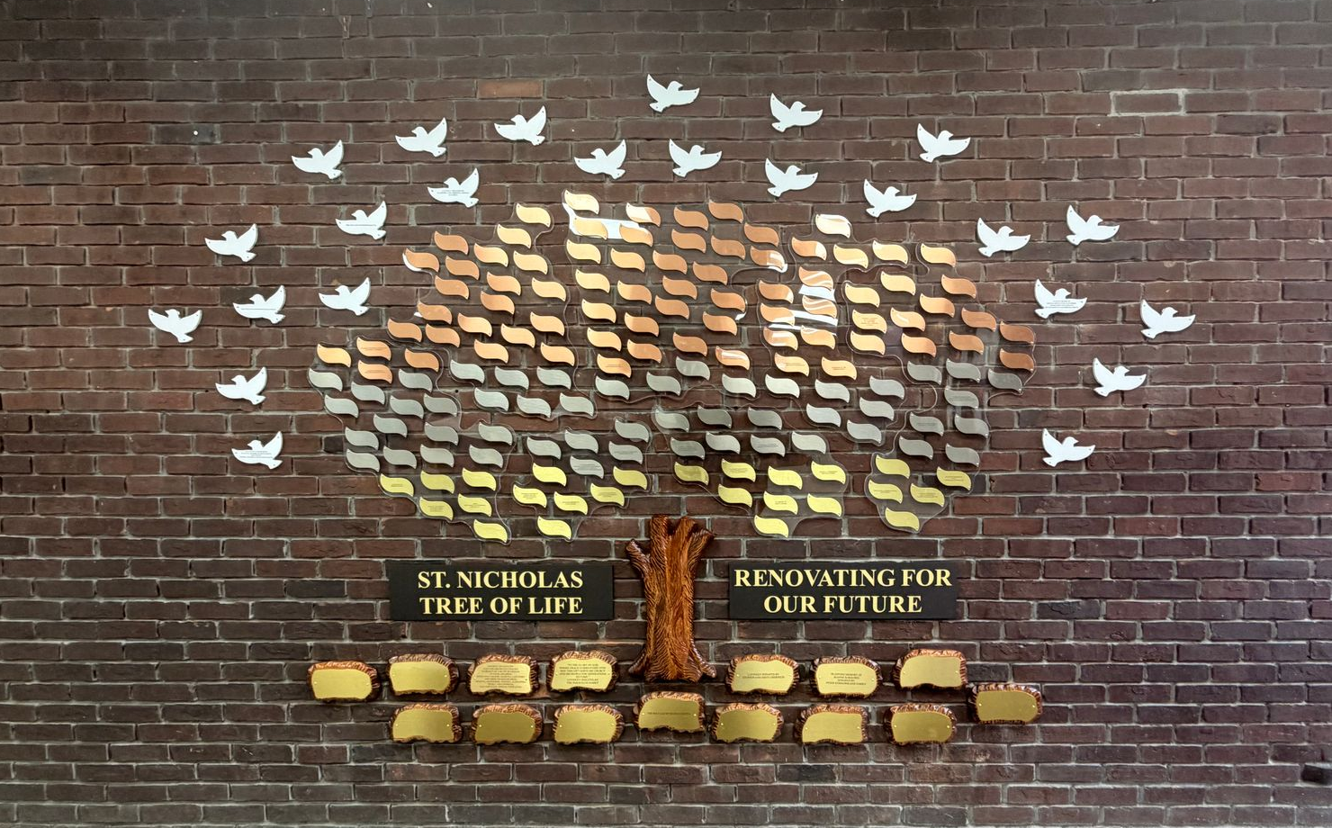 Mosaic wall art of a glowing tree with white birds on a brick wall in a hallway