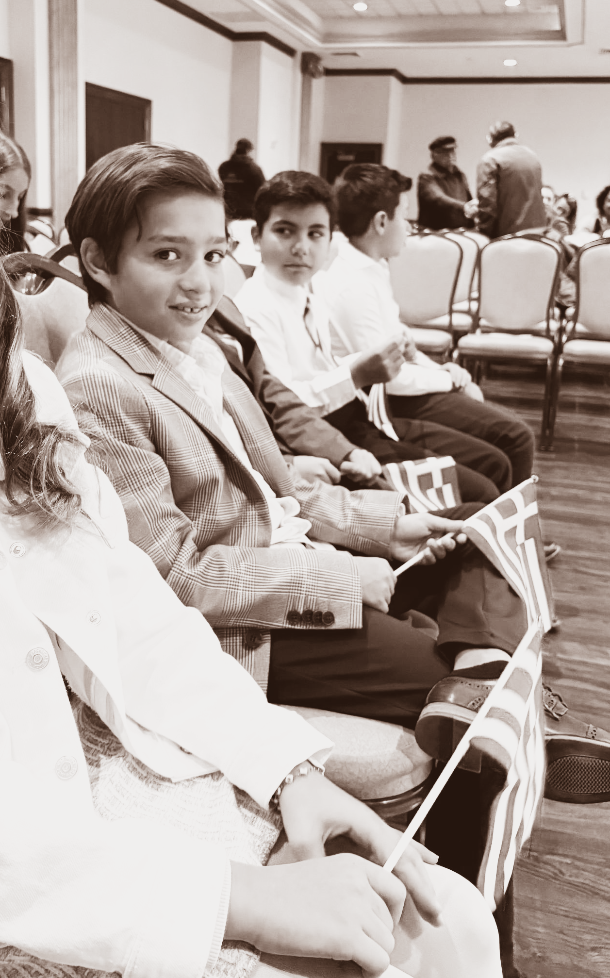 People seated in a meeting room, smiling and holding papers, with empty chairs in the background.