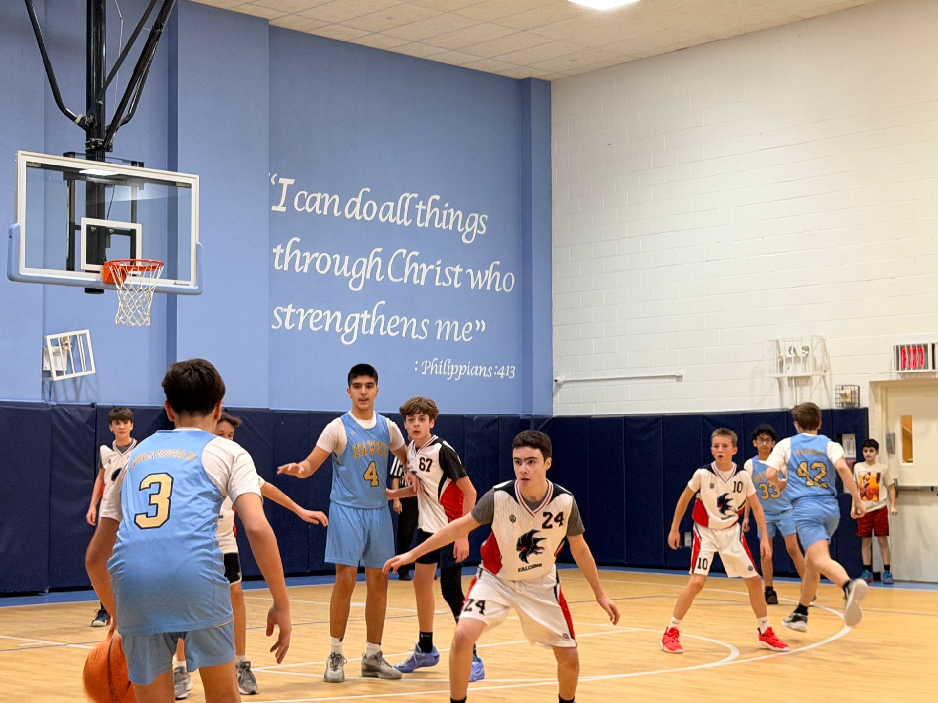 Youth basketball game in a gym, players in light blue and white jerseys competing near the hoop.