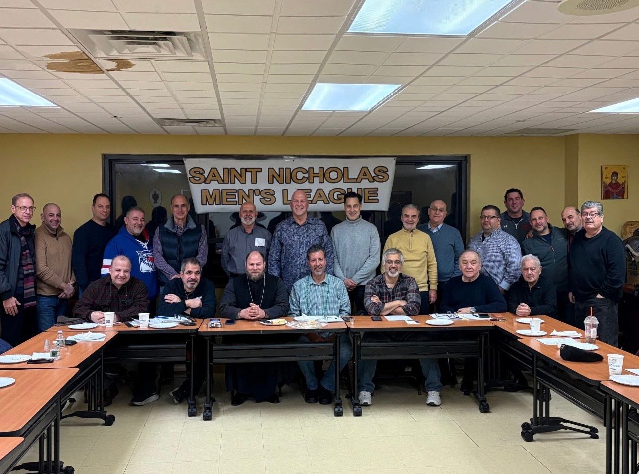 Group photo of people seated and standing in a conference room with a “Saint Nicholas News” banner behind them