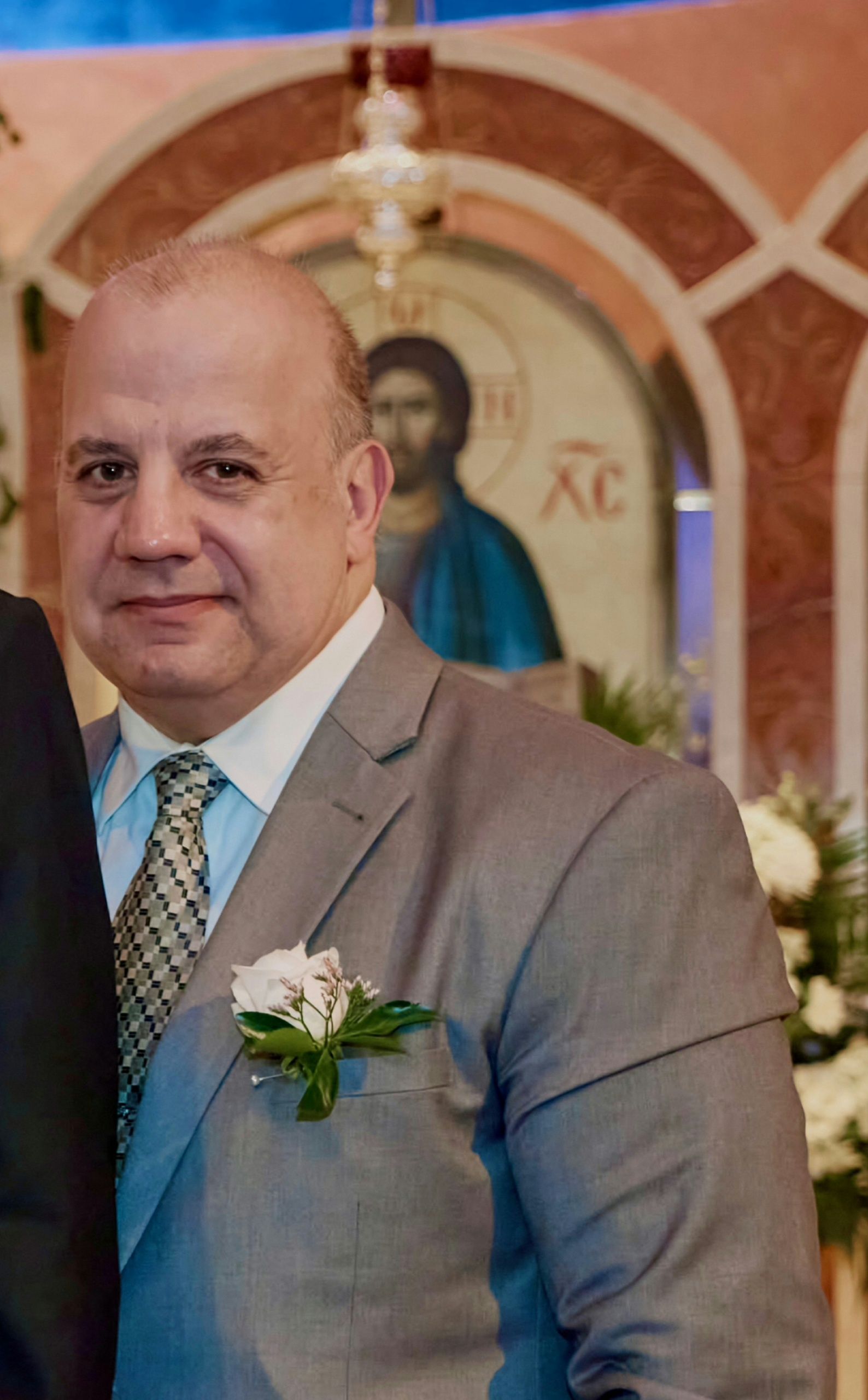 Man in a tan suit with boutonniere standing before a church icon backdrop