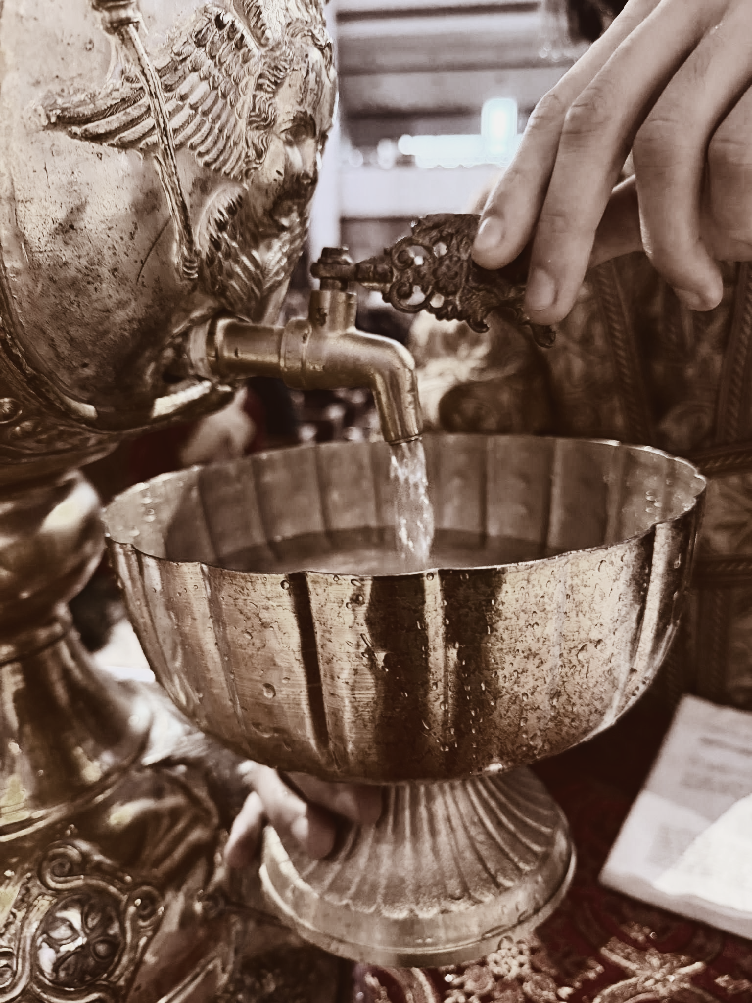 Hands pouring liquid into a decorative metal bowl on a table
